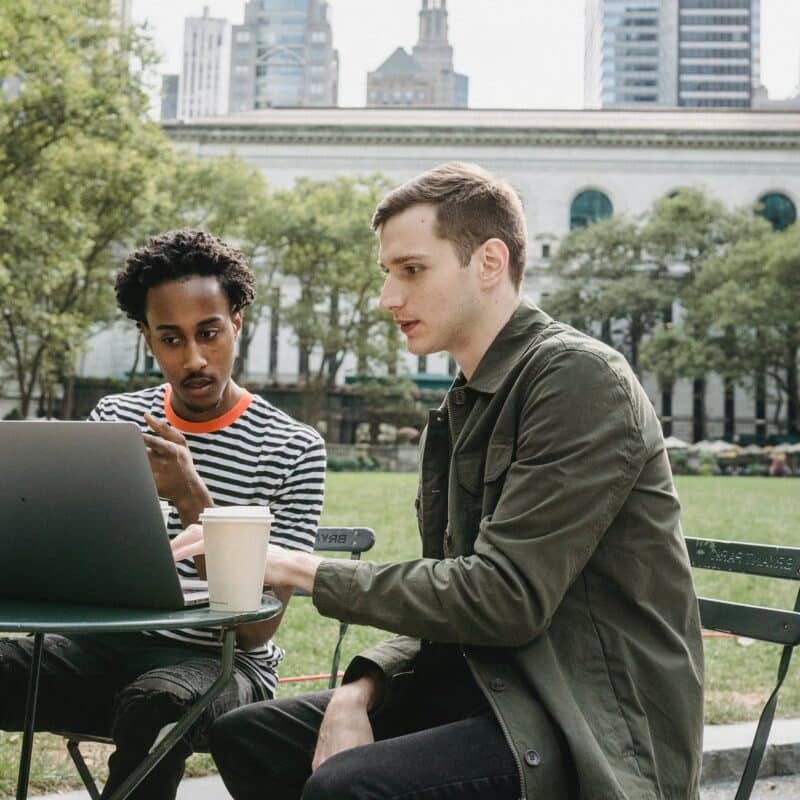 concentrated young multiracial colleagues working distantly on laptop in park